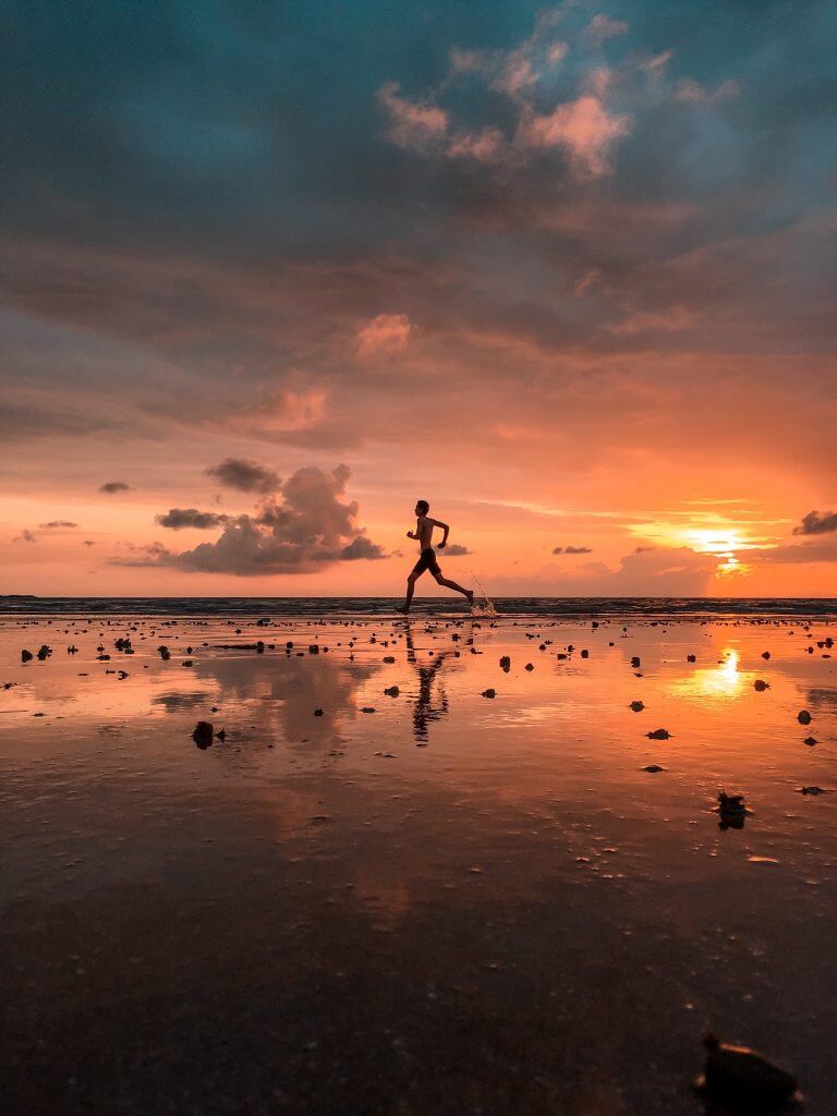 An athlete running along a beach at sunset